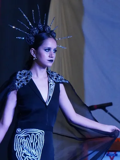 A model in a dark, glamorous outfit with an intricate headpiece from an avant-garde collection.