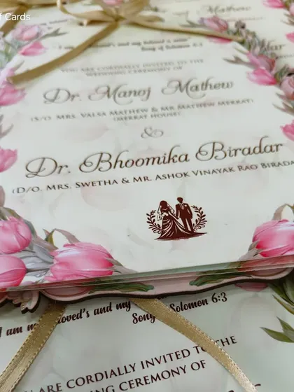 A close-up of a die-cut invitation framed with pink tulips, showcasing a modern Christian wedding design tied with a golden ribbon.
