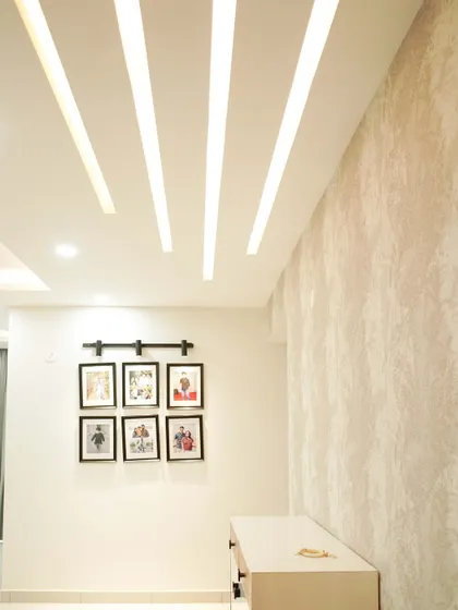 A living room wall featuring framed family photos and subtle striped lighting on the false ceiling, adding a personal and modern touch.