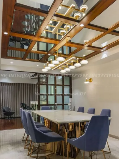 We designed this dining space with a dramatic coffered ceiling featuring wood and mirror panels. The large marble-topped table is surrounded by plush blue velvet chairs, creating a formal and opulent setting for meals.