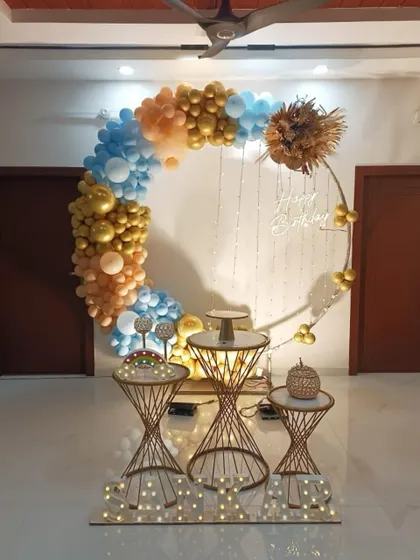 A simple yet elegant indoor setup with a circular balloon arch in blue and gold. The decoration includes modern dessert stands and fairy lights for a touch of sparkle.