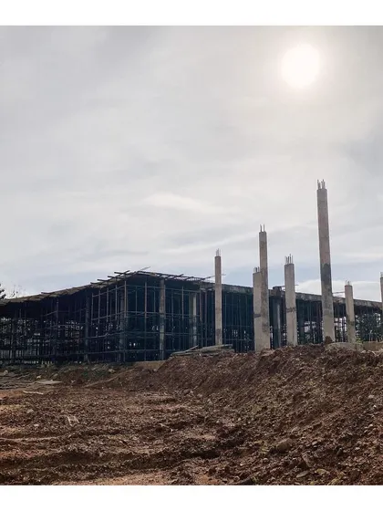 The steel framework of the main building under construction, with concrete pillars rising from the earth. This image documents the early stages of the project, showing the bones of the structure before the walls were added.
