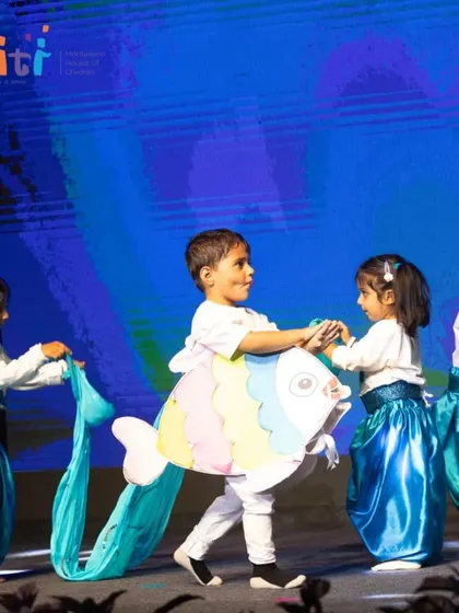 Children representing Neera (Water) perform on stage. The costumes include a large fish and flowing blue fabric to simulate waves.
