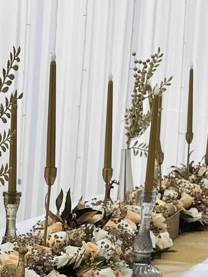 A close-up of the table setting, showing the tall golden candles and delicate floral arrangements.