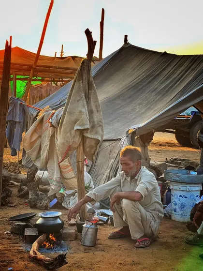 A man cooking over an open fire next to his makeshift tent at the Pushkar Fair, showcasing the rustic life of the traders.