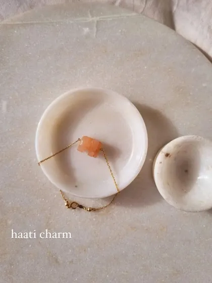A close-up of the Peach Moonstone 'haati' charm on a bracelet.