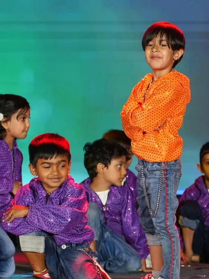 A group of children in purple and orange costumes strike a pose during their Annual Day performance.
