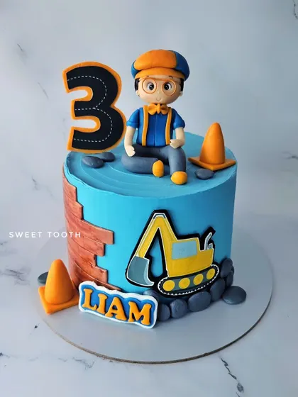 A Blippi-themed cake for Liam's 3rd birthday. This chocolate and strawberry cake features a hand-sculpted Blippi figurine and construction elements like an excavator.