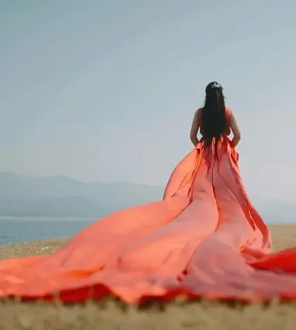 A serene and powerful shot from behind, showing the bride looking out over the water. The immense red trail spreads out, symbolizing the start of a grand new journey.
