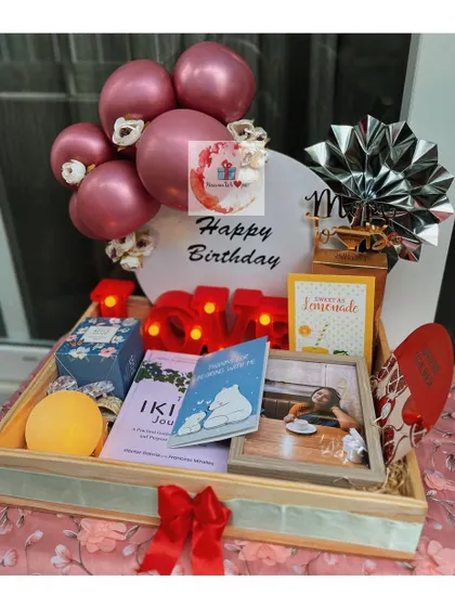 A stunning birthday tray curated for her, featuring a personalized LED initial, a mini balloon bouquet, framed photos, and a collection of her favorite treats and self-care items.
