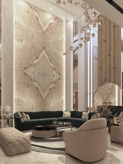 A breathtaking view of a double-height living room, where a massive book-matched marble slab creates a stunning focal point. The space is furnished with a plush green L-shaped sofa and elegant accent chairs.