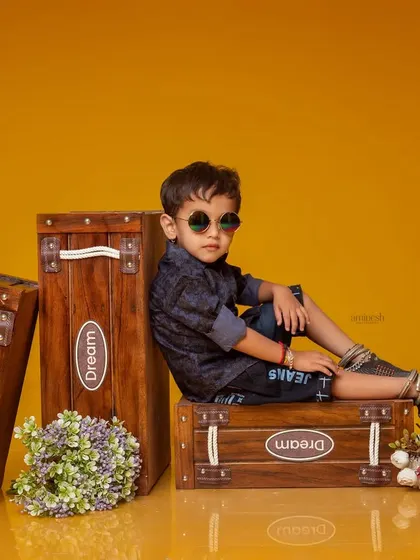 A cool and stylish pre-birthday portrait of a young boy. He is sitting on wooden boxes with sunglasses, posing like a little star for his studio photoshoot.