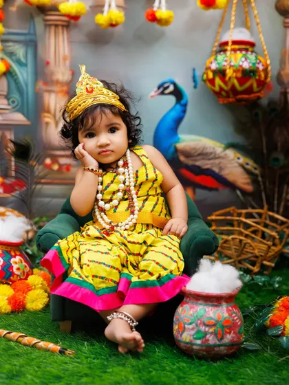 A thoughtful little Radha rests her head on her hand, looking absolutely adorable in her yellow dress.