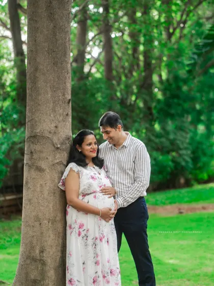A candid family shot by a tree, capturing a natural and loving interaction between the parents and their daughter during their maternity session.