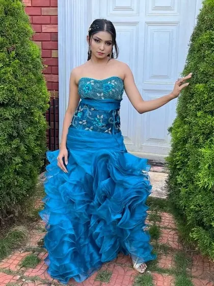 A full-length view of the blue ruffled bodycon gown. The strapless design and form-fitting silhouette make it a chic and fashionable choice.