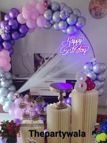 A purple, pink, and silver balloon ring with a 'Happy Birthday' neon sign.