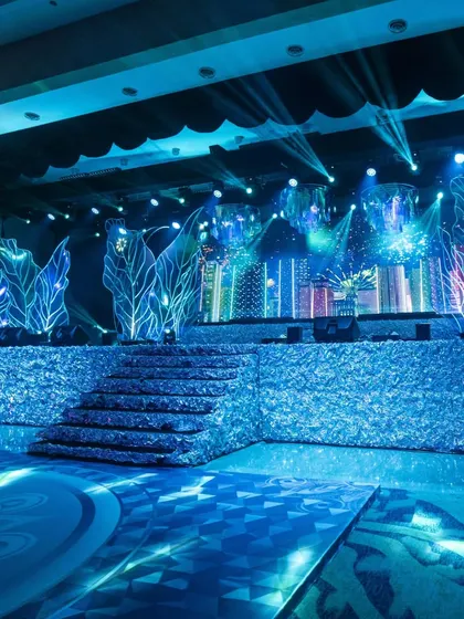 A wider view of the empty Sangeet stage, showing the central steps, the custom floor graphics, and the full expanse of the iridescent and LED backdrop. This highlights the scale and detail of our design before the party begins.