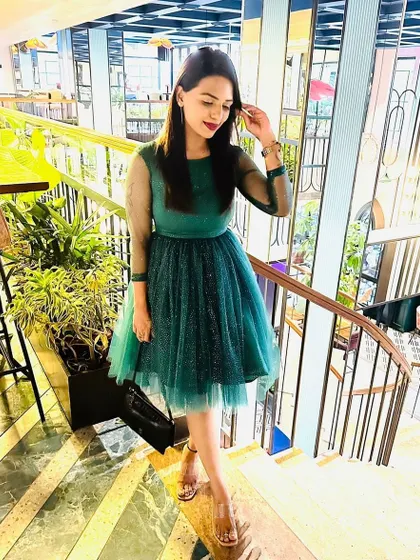 Pooja looks gorgeous in this custom-made emerald green party dress. The design features sheer sleeves and a layered tulle skirt with subtle polka dots, perfect for a birthday or cocktail event.