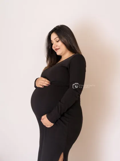 A gentle and classic portrait in a black dress against a plain background. This timeless shot focuses on the quiet joy of expecting.