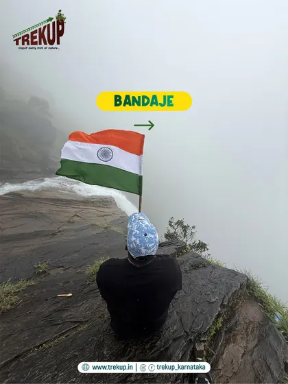 A trekker sits peacefully at the edge of Bandaje falls with the flag. It is a moment of quiet reflection and pride.