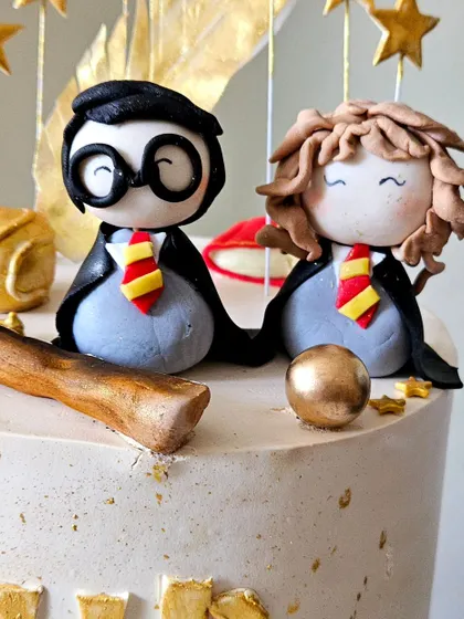 A magical Harry Potter birthday cake. This whipped cream cake is decorated with gold accents and features handmade figurines of Harry and Hermione.