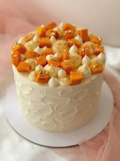 A celebration of mango season. This cake has a textured buttercream finish and is topped with fresh mango chunks, macarons, and a sprinkle of gold leaf.
