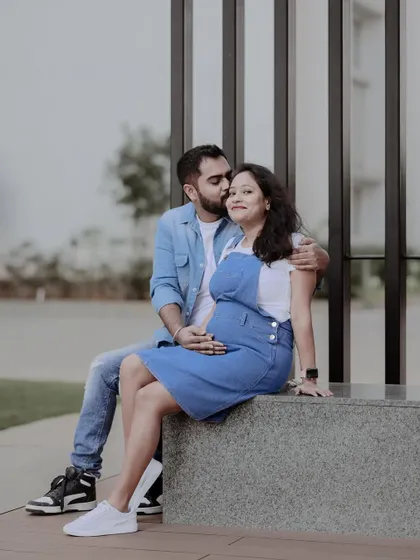 A sweet and intimate moment from a casual maternity session. The partner gently kisses the expecting mother's cheek as they sit together outdoors, showcasing their connection.