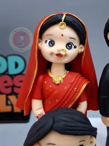 A close-up of the bride figurine for a custom wedding cake, showcasing the intricate details of her red saree and jewelry.