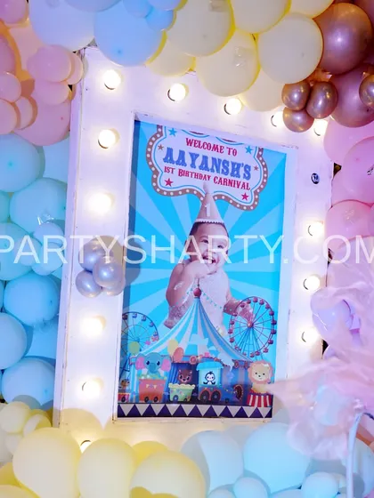 A personalized welcome sign for a carnival-themed first birthday, framed with lights and surrounded by soft pastel balloons.
