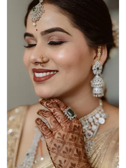 A close-up showcasing the flawless makeup and intricate henna design. The soft smokey eye and matte terracotta lip color add a modern touch to her traditional attire.