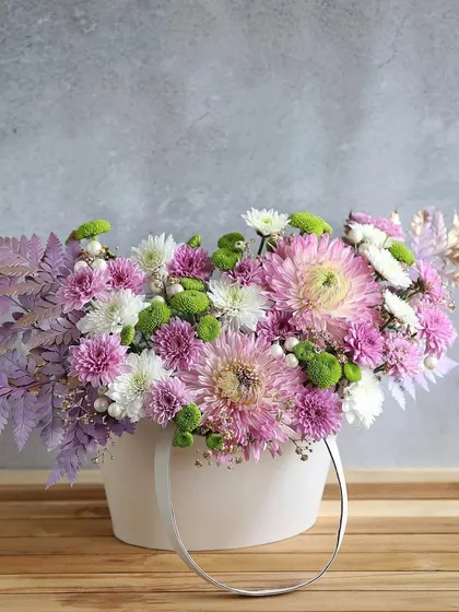 A chic arrangement of purple and white chrysanthemums in a modern white carry-bag vase, a stylish gift for any occasion.
