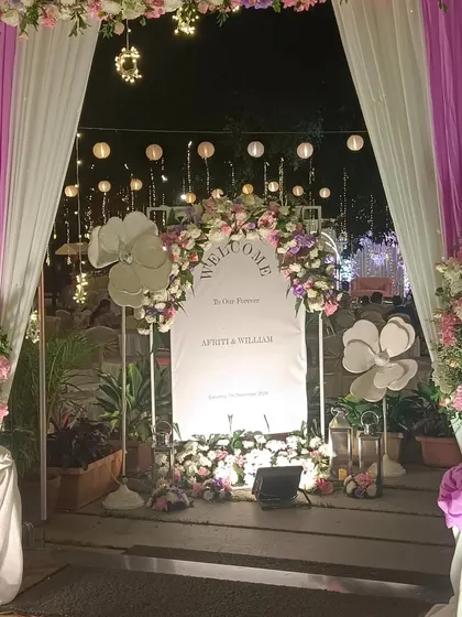 A modern and chic entrance for a reception, with white and purple drapes, a welcome sign, and oversized paper flowers.
