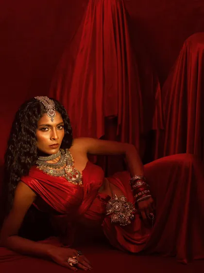 A reclining pose that showcases the intricate jewelry against a rich, textured background. The composition is both elegant and dramatic.