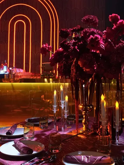 A moody and romantic tablescape from the theatre-themed Sangeet. The deep red florals, personalized napkins, and glowing candles set against a neon-lit bar created a dramatic and intimate dining experience.