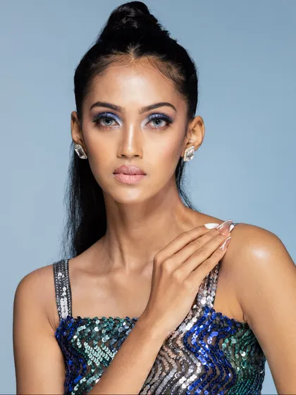 A close-up beauty portrait of a model in a sequin dress, highlighting her striking blue eye makeup.