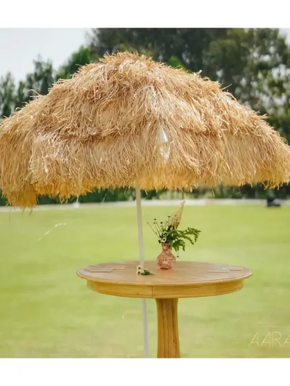 A rustic hay-thatched umbrella provides a charming, natural touch to this outdoor brunch setup. It's a perfect example of how we use sustainable materials to create a unique and stylish ambiance.
