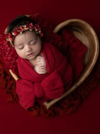 All you need is love. This newborn girl is wrapped in a rich red swaddle and placed in a heart shaped wooden bowl, creating a bold and beautiful statement portrait.