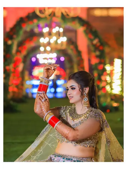 A close-up of the bride, capturing a dance pose. This shot highlights her intricate blouse, red choora bangles, and joyful expression.