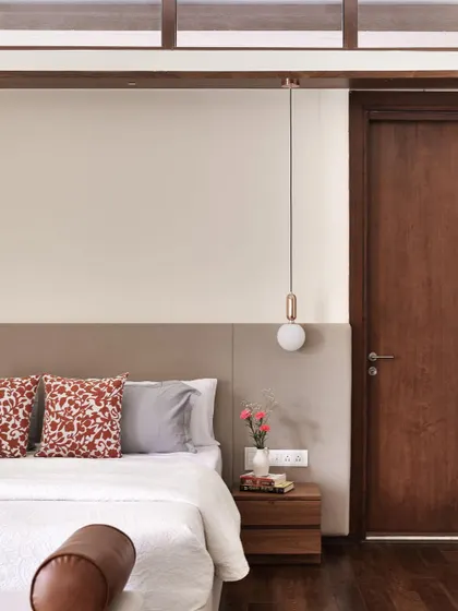 A detail of the bedside in the 'A Walk in the Clouds' primary room, with a simple upholstered headboard, a warm wooden nightstand, and a delicate pendant light.