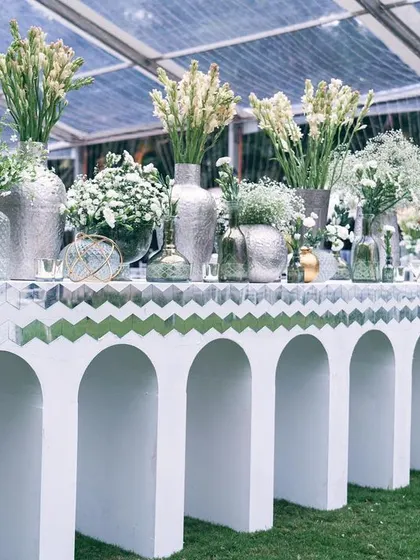 A bar station decorated with an array of white flowers in silver and glass vases. Even functional areas are designed to be beautiful and cohesive with the overall theme.