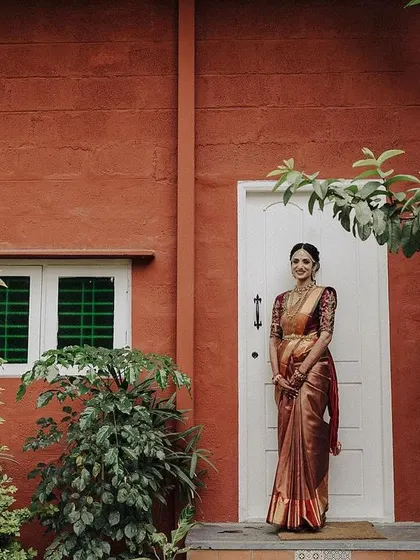 A bride standing in front of a striking red-orange wall. The contrast of the vibrant wall with the surrounding greenery makes for a bold and beautiful bridal portrait.
