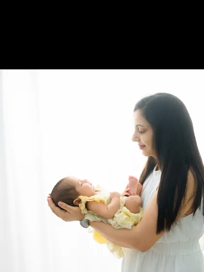 A mother holds her sleeping baby, who is dressed in a sunny yellow outfit. The soft, bright light creates an angelic and peaceful mood.
