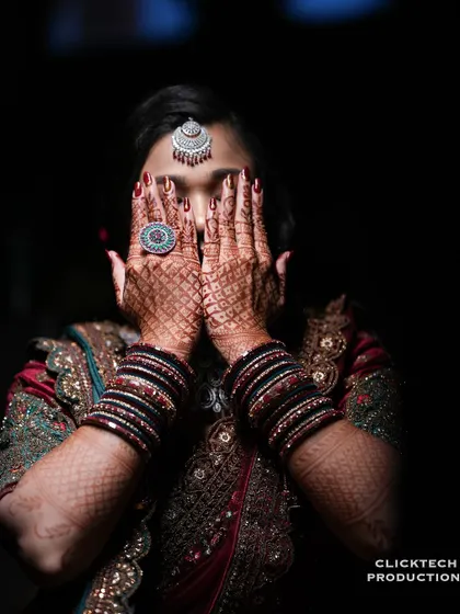 An artistic shot of the bride hiding her face behind her henna-covered hands, focusing on the intricate details and jewelry.