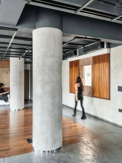 This view highlights the interplay of materials, from the smooth, cylindrical concrete column to the warm wood paneling of the reading nook. The design balances raw industrial elements with refined details to create a tactile and visually layered environment.