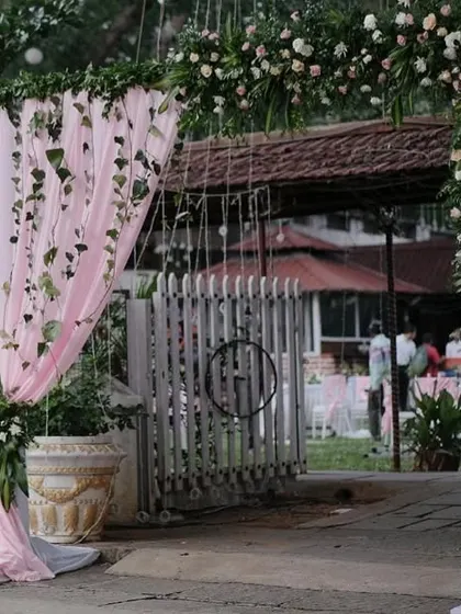 A beautiful floral archway at the entrance to an outdoor wedding, featuring soft pink draping and an abundance of pink and white flowers.