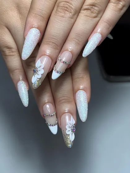 A truly show-stopping set of stiletto nails. The design includes a mix of glitter, 3D flowers, and chains of rhinestones for a high-glam, bridal look.