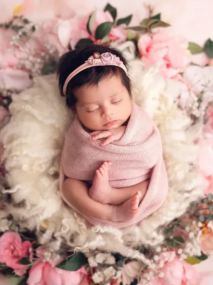 A beautiful overhead shot of a newborn girl in a pink swaddle, nestled in a fluffy white nest and surrounded by pink and white peonies.