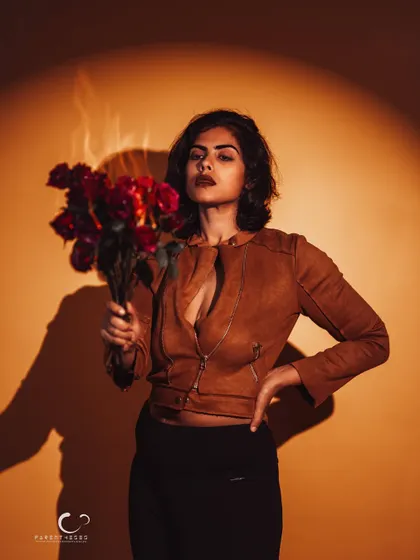 A dramatic portrait using a single spotlight. The contrast between the warm light, the dark shadows, and the red roses creates a powerful and theatrical image.