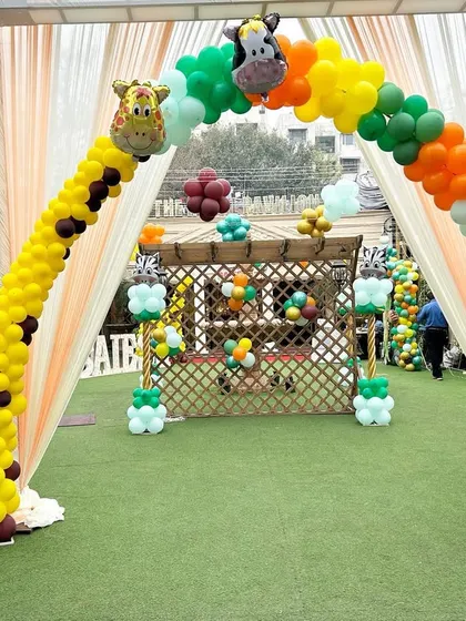 A creative entrance arch for a jungle-themed party. The arch is designed to look like a giraffe's neck and leads to a smaller photo booth area.