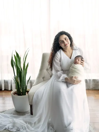 A mother holds her newborn in a beautiful, light-filled portrait. The flowing white dress and bright background create an ethereal, angelic feel for this special moment.